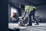 Construction worker using a power cutter indoors, with a dust extractor in the background.