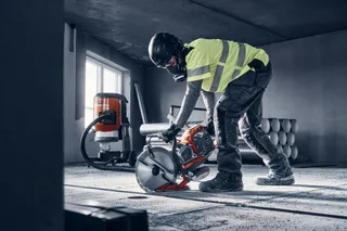Construction worker using a power cutter indoors, with a dust extractor in the background.
