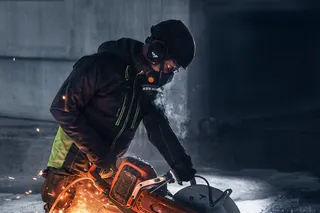 A construction worker using a power cutter to cut metal, with sparks flying in a dimly lit setting.
