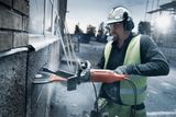 A construction worker using a power cutter on a brick wall outdoors.