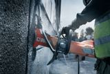 A construction worker using a power cutter on a concrete wall.