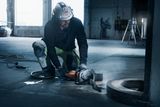 A worker kneeling and using a power cutter on a concrete floor.