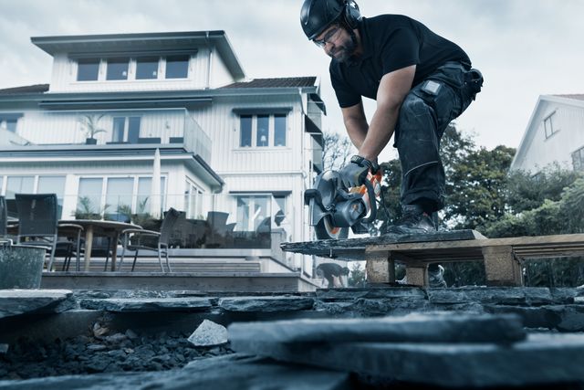 A construction worker using a power cutter on a stone surface in a residential area.