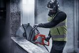 Construction worker using a power cutter on a concrete wall.