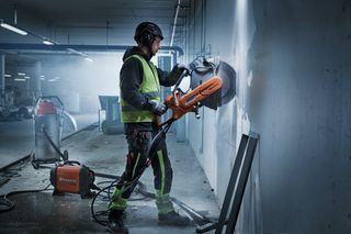 Pracownik budowlany używający przecinarki na ścianie na placu budowy w pomieszczeniu.