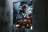 Construction worker using a power cutter on a concrete wall.