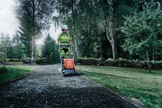 Personne utilisant un compacteur à plaque compacte sur un chemin de gravier dans un jardin.