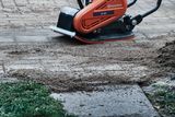 Een trilplaat van Husqvarna die de grond op een verharde ondergrond gladstrijkt.