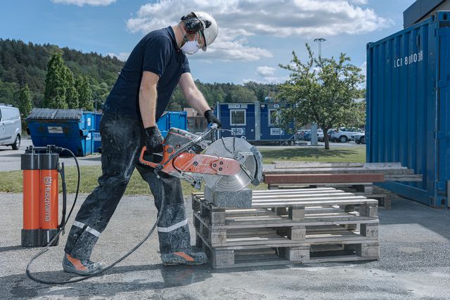 A construction worker using a power cutter on a stack of wooden pallets outdoors.