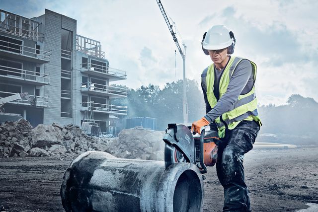 Construction worker using a power cutter on a concrete pipe at a construction site.