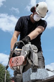 Ένας εργάτης οικοδομής χρησιμοποιεί έναν κόφτη ρεύματος για να κόψει πέτρα σε εξωτερικούς χώρους, φορώντας προστατευτικό εξοπλισμό.