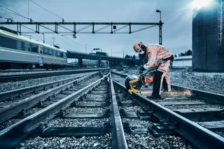 A construction worker using a power cutter on railway tracks.