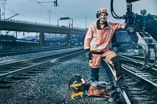 A construction worker standing on railway tracks next to a power cutter.