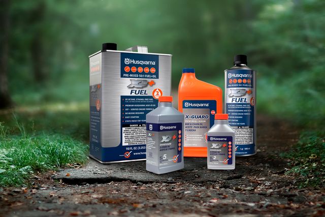 A collection of Husqvarna fuel and oil products displayed on a forest path.