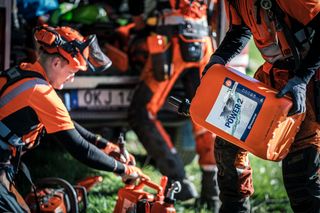 Arbetare som hanterar motorsågar och en bränslebehållare utomhus.