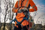 A person wearing work gear with climbing ropes and harness in an outdoor setting.