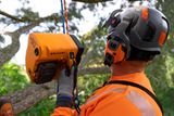 Uma pessoa usando equipamento de trabalho e capacete operando um dispositivo em um ambiente de árvore.