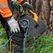 Uma pessoa usando uma ferramenta de escalada com uma corda presa, de pé ao lado de uma árvore.