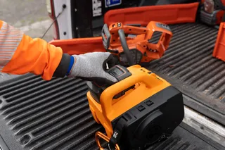 Uma pessoa usando luvas de trabalho manuseando uma ferramenta elétrica em uma cama de caminhão.