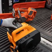 Uma pessoa usando luvas de trabalho manuseando uma ferramenta elétrica em uma cama de caminhão.