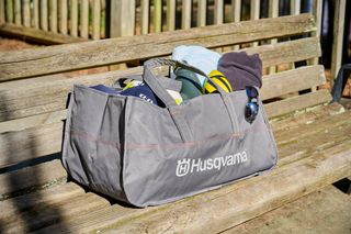 A Husqvarna branded bag on a wooden bench, filled with various items including a towel and sunglasses.