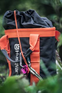 Uma mochila da marca Husqvarna com correias cor de laranja colocada num ambiente florestal.