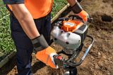 A person operating a Husqvarna earth auger in a garden setting.