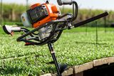 A power auger with a spiral drill bit positioned on the edge of a grassy area, ready for use.