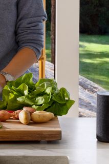 Una persona que prepara verduras en una cocina con un robot cortacésped funcionando en el exterior, en el césped.