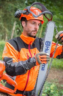 Una persona con equipo de trabajo ajustando la cadena de una motosierra Husqvarna en un árbol caído en un bosque.