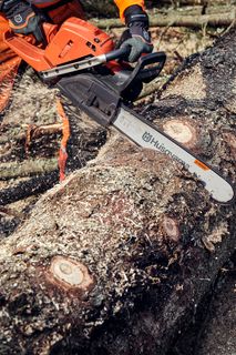 A person using a Husqvarna chainsaw to cut a large tree log outdoors.