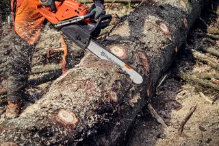 A person using a Husqvarna chainsaw to cut a large tree log outdoors.