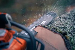 Närbild av en motorsåg som skär genom en trädstock med flygande sågspån.