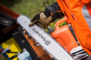 Una persona che tiene in mano una barra per motosega Husqvarna, circondata da vari accessori e strumenti per motosega.