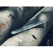 Lišta motorovej píly Husqvarna spočívajúca na rezaných kmeňoch stromov s kôrou.