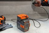 Людина заряджає акумуляторний блок Husqvarna на верстаку, тримаючи поруч захисне спорядження.