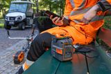 A person sitting on a bench using a smartphone with a Husqvarna battery and trimmer nearby.
