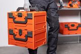 A person carrying two stacked toolboxes in a workshop setting.