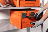 A person placing an orange storage box on a shelf, wearing gloves.