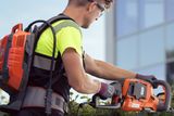 A person using a hedge trimmer to trim bushes in a garden setting.