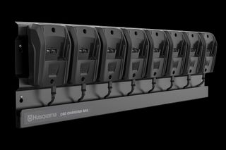 A Husqvarna charging rail with eight battery chargers mounted on it.