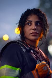 En person klädd i arbetskläder med reflexer och handskar som står utomhus i skymningen.