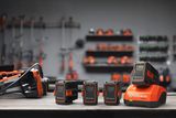 Un ensemble de batteries Husqvarna et un chargeur sur un établi, avec des outils suspendus à l’arrière-plan.