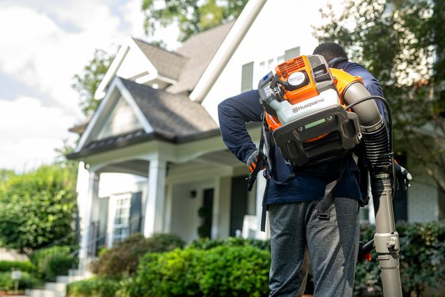 A person using a backpack leaf blower to clear leaves in a residential area.