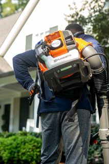 A person using a backpack leaf blower to clear leaves in a residential area.