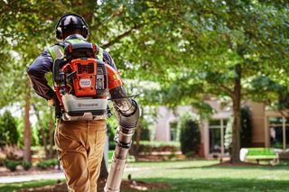 A person using a backpack leaf blower in a park setting.