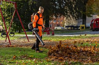 Una persona usando un soplador de hojas para limpiar hojas caídas en un parque.