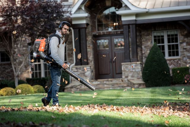 A person using a leaf blower to clear fallen leaves in a residential garden.
