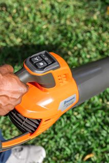 A person holding a leaf blower on a grassy area, showcasing the control panel.