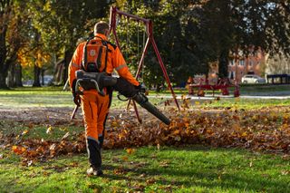 在公园环境中使用吹叶机清除落叶的人员。